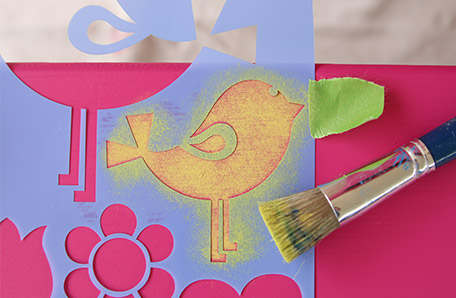 Hold the stencil to the dresser with painter’s tape then dab it with a stencil brush