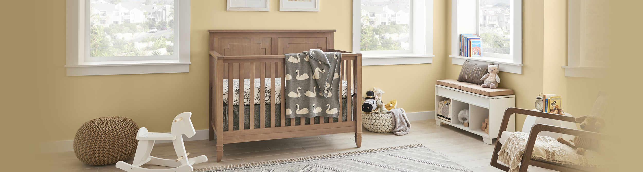 Inspirational youth nursery room image with yellow wall and white trim, brown wooden crib with white rocking horse.