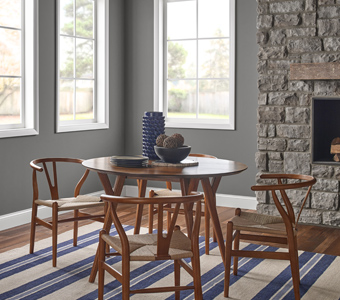Gray dining room with wooden table set, big windows and a stone fireplace.