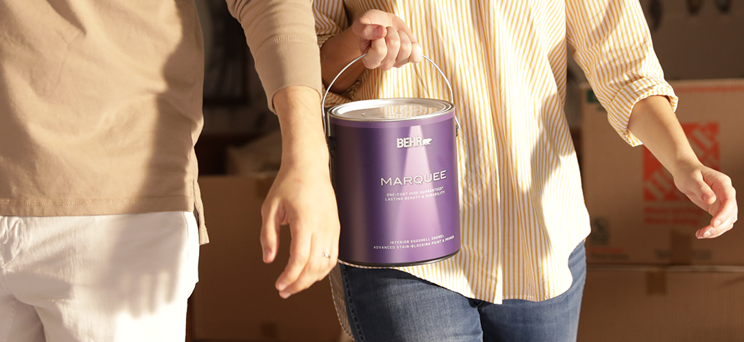 Two people walking with one of them holding a can of Behr paint