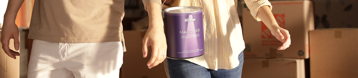 Two people walking with one of them holding a can of Behr paint