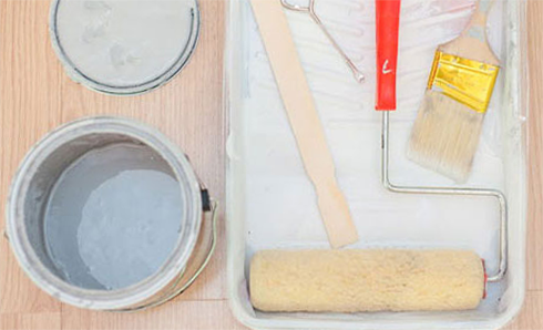 Paint roller and paint brush laying in a paint tray next to a paint can and lid