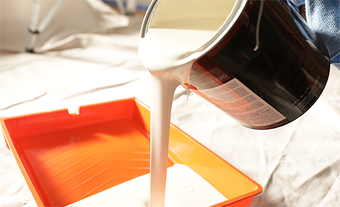 White paint pouring out a paint can into a paint tray